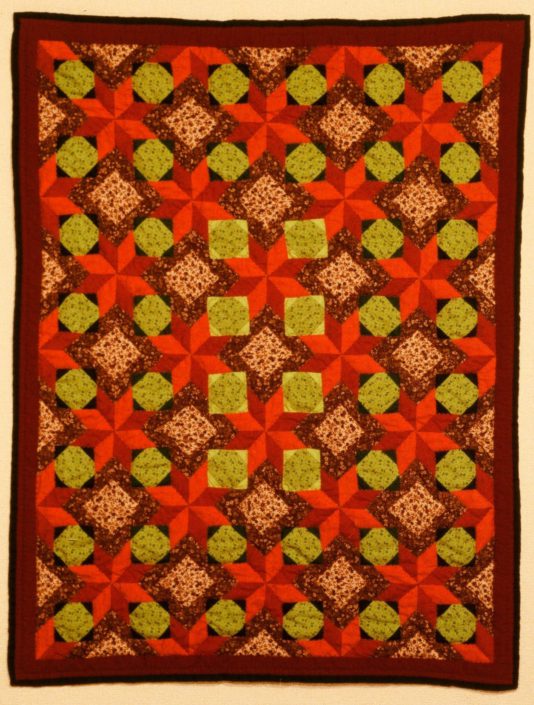 A colorful quilt with red, orange and green designs.